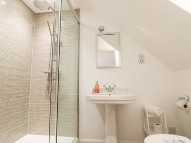 A bathroom with a shower enclosure a pedestal sink with a mirror above and a small shelf with towels and toilet paper at The Bath House in Blockley