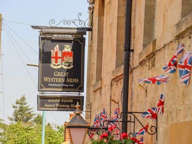 A pub sign for Great Western Arms with British flags on a stone building wall at The Bath House in Blockley