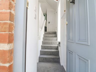 A carpeted staircase leading to a closed white door with white walls and a partially open blue door at The Bath House in Blockley