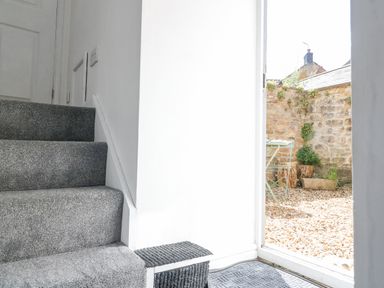 A carpeted staircase next to an open door leading to a small outdoor area with gravel and stone walls at The Bath House in Blockley
