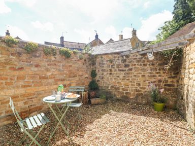 An outdoor patio with stone walls gravel floor a small table and two chairs with breakfast items at The Bath House in Blockley