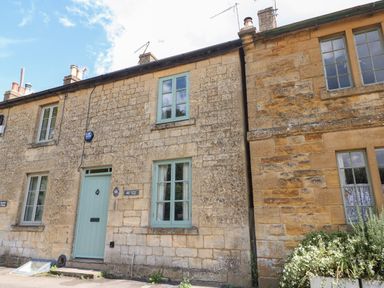 Stone cottage with three windows light blue door and plants outside at Red Fawn Cottage in Blockley
