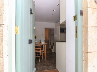 View through an open front door into a kitchen dining area with a table set for breakfast and a staircase in the background at Red Fawn Cottage in Blockley