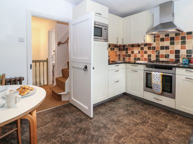 A kitchen with white cabinets a tiled backsplash a built in oven and microwave and a table with plates and croissants at Red Fawn Cottage in Blockley