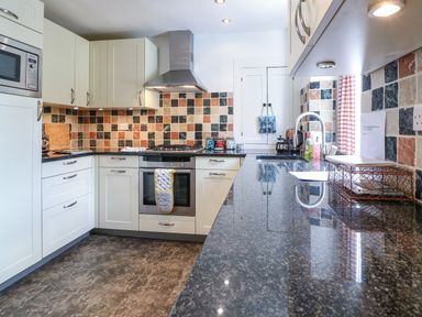 A kitchen with white cabinets a tiled backsplash a stove a microwave and a countertop at Red Fawn Cottage in Blockley