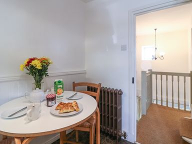 A small dining area with a round table set with croissants jam teapot juice and flowers near a staircase at Red Fawn Cottage in Blockley