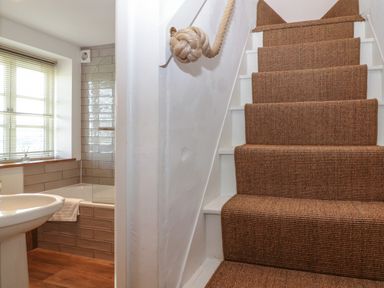 A staircase with carpet and a rope handrail next to a bathroom with a sink and a bathtub at Red Fawn Cottage in Blockley