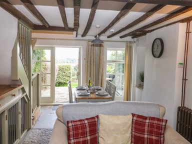 A living room with a sofa and dining table set near glass doors leading to a garden at Red Fawn Cottage in Blockley