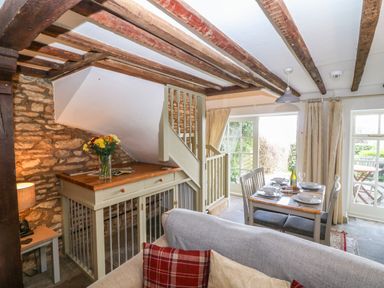 A dining area with table set for four and a wooden cabinet under stairs in a room with exposed wooden beams at Red Fawn Cottage in Blockley