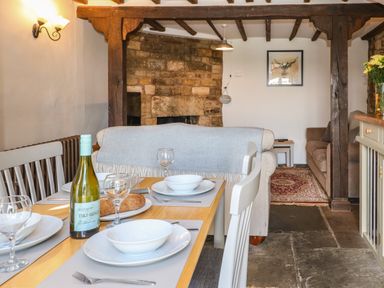 A dining table set with plates glasses and a wine bottle in a living area with a stone fireplace and sofas at Red Fawn Cottage in Blockley