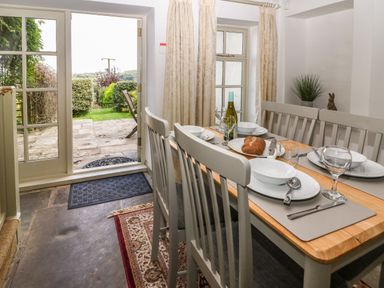 A dining area with a wooden table set with plates glasses and a bottle of wine next to glass doors leading to a garden at Red Fawn Cottage in Blockley