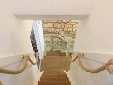 A narrow staircase with rope handrails and carpeted steps leading down to a landing with a stone wall at Red Fawn Cottage in Blockley