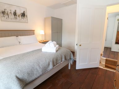 A bedroom with a bed with white bedding and gray blanket and rolled towels a nightstand with a lamp a wardrobe and open door showing stairs at Red Fawn Cottage in Blockley