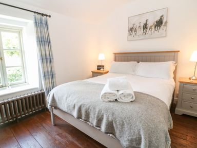 A bedroom with a bed folded towels bedside tables lamps and a window with curtains at Red Fawn Cottage in Blockley