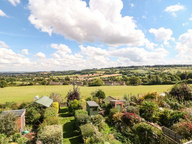 A garden with sheds and bushes overlooking fields and hills at Red Fawn Cottage in Blockley