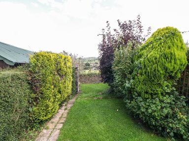 A garden path with grass and hedges on both sides leading to a stone wall at Red Fawn Cottage in Blockley