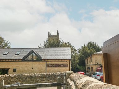 A stone building with a shop and cafe sign near a stone wall and parked cars in a village