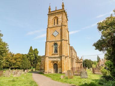 A stone church tower with a clock surrounded by gravestones and greenery at Red Fawn Cottage in Blockley