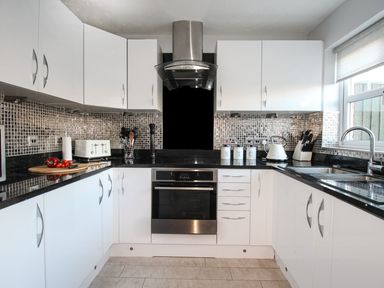 A kitchen with white cabinets black countertops and a stove at Beach View House in Wyke Regis