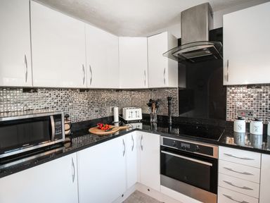 A kitchen with white cabinets black countertops a microwave toaster stove and kitchen utensils at Beach View House in Wyke Regis