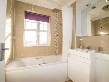 A bathroom with a bathtub shower curtain sink and mirror at Beach View House in Wyke Regis