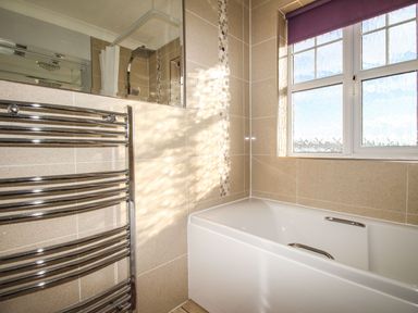 A bathroom with a bathtub a window a heated towel rail and a shower area at Beach View House in Wyke Regis