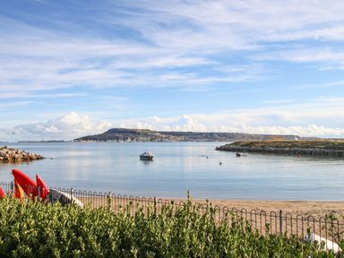 A view of a calm bay with a small boat in the water and kayaks on the shore at Beach View House in Wyke Regis