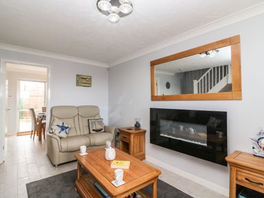 A living room with a beige sofa wooden coffee table side tables a wall-mounted fireplace and a large mirror at Beach View House in Wyke Regis