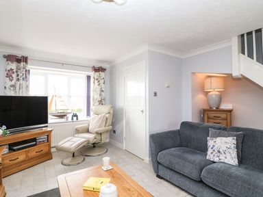 A living room with a TV on a wooden stand a beige recliner chair a blue sofa and a wooden coffee table at Beach View House in Wyke Regis