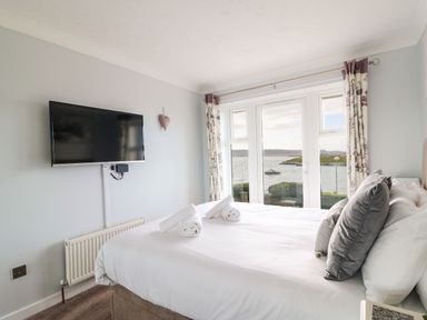 A bedroom with a bed, rolled towels, a wall-mounted TV, and windows overlooking a body of water at Beach View House in Wyke Regis