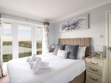 A bedroom with a bed with pillows and rolled towels next to a window with a water view at Beach View House in Wyke Regis
