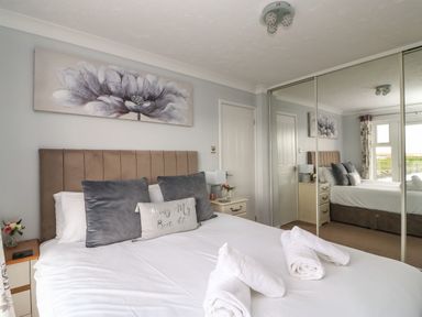 A bedroom with a bed pillows and towels beside mirrored wardrobes at Beach View House in Wyke Regis