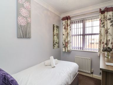 A small bedroom with a single bed a window with floral curtains and vertical blinds a radiator and a dressing table at Beach View House in Wyke Regis