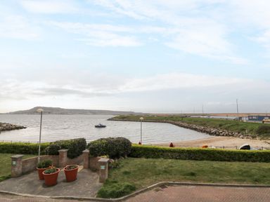 A waterfront view with a small boat on the water and a grassy area with potted plants at Beach View House in Wyke Regis