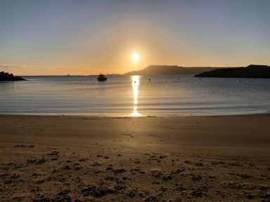 A beach with sand in the foreground and a boat on calm water with the sun setting behind hills at Beach View House Wyke Regis