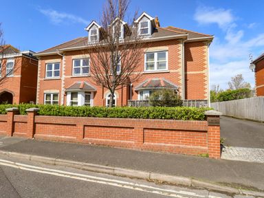 A two story brick residential building with dormer windows and a hedge in front at Marina Reach in Weymouth