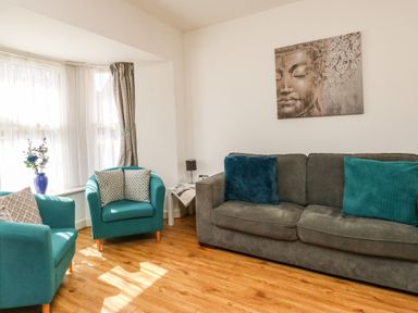 A living room with two teal armchairs and a grey sofa with cushions and a Buddha painting on the wall at Marina Reach in Weymouth