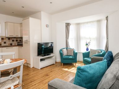 A living room with teal armchairs a gray sofa a television and a kitchen area at Marina Reach in Weymouth