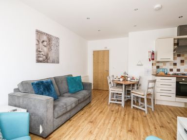 A living room with a gray sofa and dining table with chairs near a kitchen area at Marina Reach in Weymouth