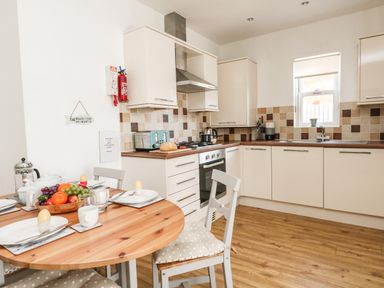 A kitchen with white cabinets a wooden dining table set with breakfast items and a tiled backsplash at Marina Reach in Weymouth