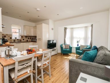 An open kitchen and living area with a dining table set for breakfast and blue armchairs by a bay window at Marina Reach in Weymouth