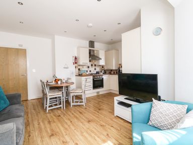 A kitchen and living area with a dining table chairs a television on a stand a blue armchair and a gray sofa at Marina Reach in Weymouth