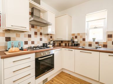 A kitchen with white cabinets a gas stove a kettle a toaster a loaf of bread on a cutting board and a sink at Marina Reach in Weymouth