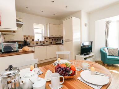A kitchen with cream cabinets a round wooden dining table set with plates eggs fruit and a French press at Marina Reach in Weymouth