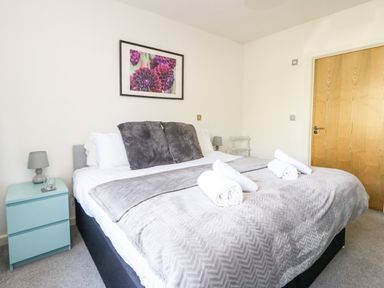 A bedroom with a double bed towels on the bed a bedside table with a lamp and a painting on the wall at Marina Reach in Weymouth