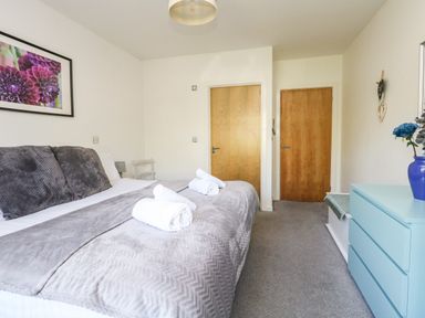 A bedroom with a double bed towels on bed blue chest of drawers and two wooden doors at Marina Reach in Weymouth