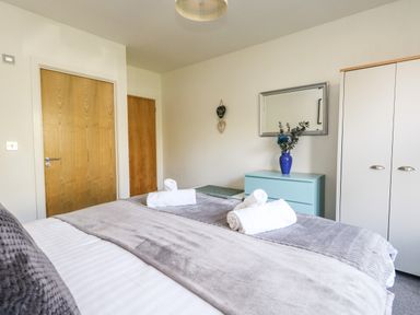 A bedroom with a bed with gray covers two wooden doors a blue dresser with a blue vase and a white wardrobe at Marina Reach in Weymouth