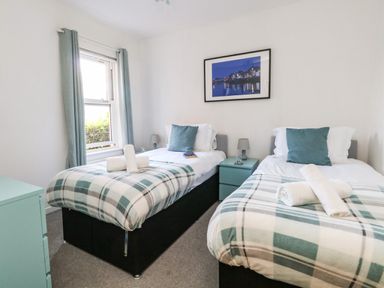A bedroom with two single beds with plaid blankets and teal cushions a window with teal curtains and a framed picture on the wall at Marina Reach in Weymouth