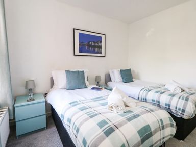 A bedroom with two single beds bedside tables lamps and a framed picture on the wall at Marina Reach in Weymouth