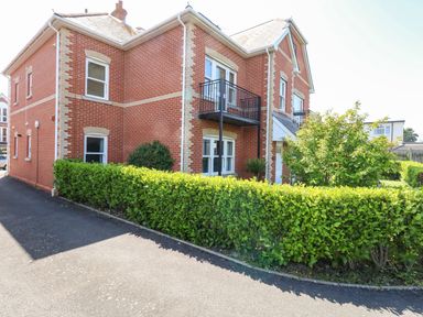A brick residential building with windows a small balcony and green hedges along the driveway at Marina Reach in Weymouth
